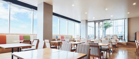 A spacious indoor area with multiple tables and chairs, large windows, and a modern design.