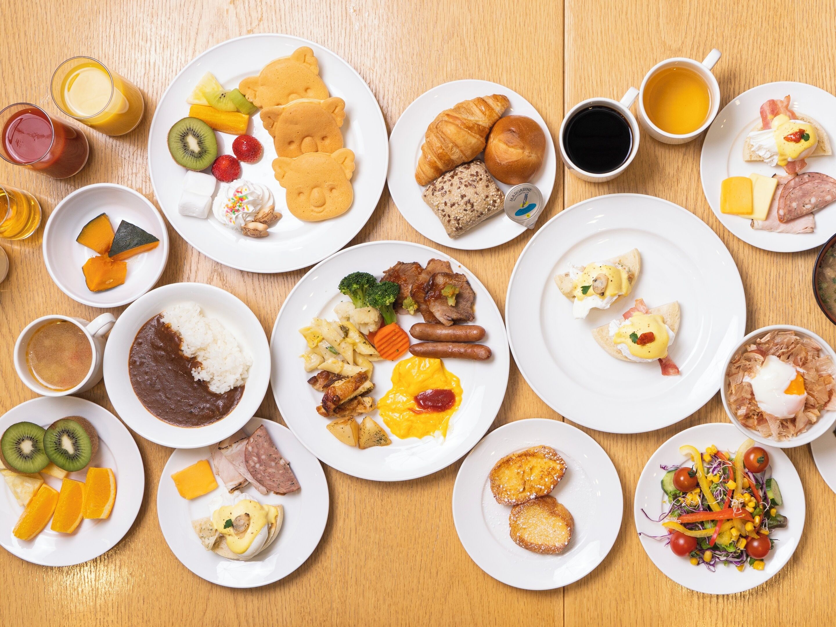 Diversos platos de desayuno como panqueques, croissants y huevos, dispuestos sobre una mesa de madera.