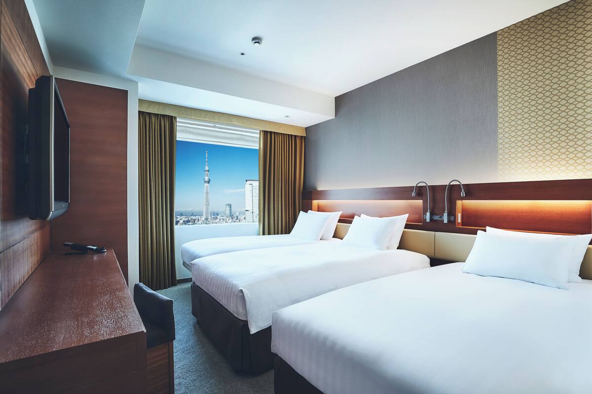 A hotel room with two beds, a desk, a TV, and a city view.