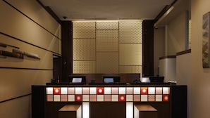 A reception desk with a patterned backdrop, a computer, and a bench. - Lotte City Hotel Kinshicho (Tokyo)