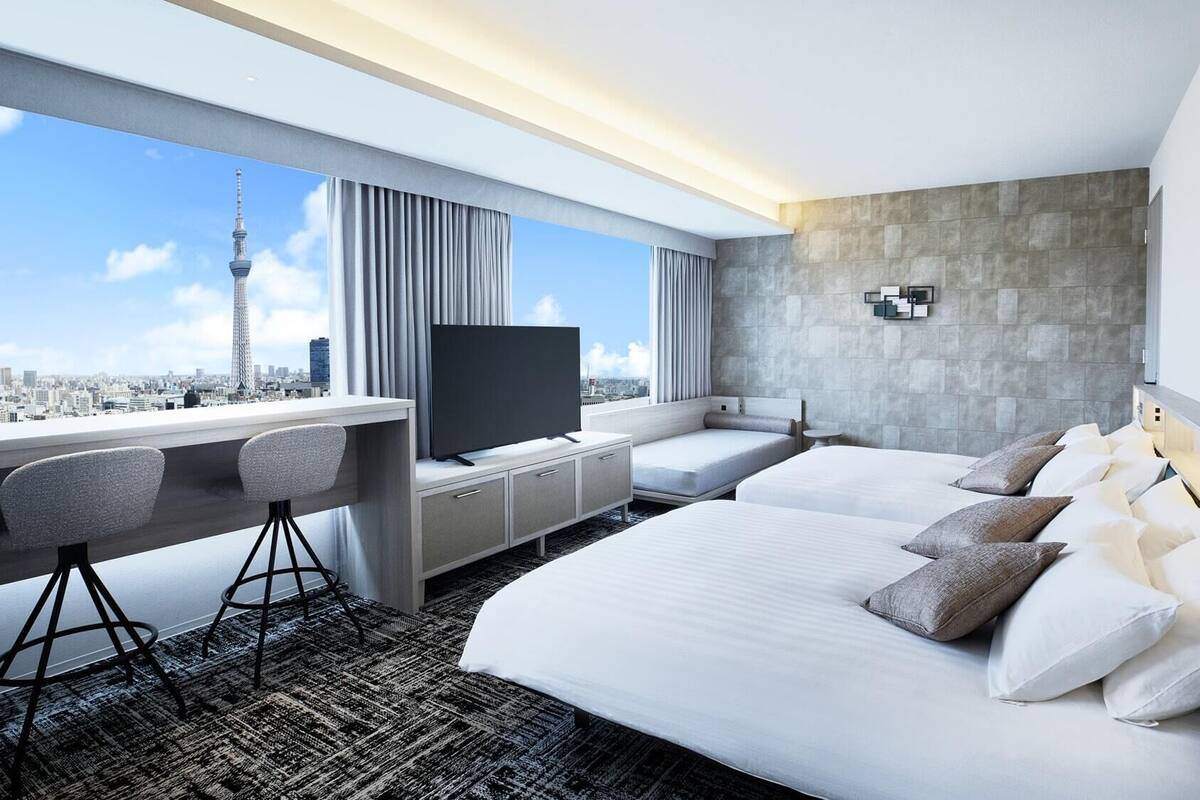 A modern hotel room with a large bed, a desk with a TV, and a city view.