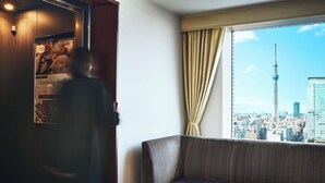 A hotel room with a large window offering a city view, a sofa, and a wooden cabinet with a poster. - Lotte City Hotel Kinshicho (Tokyo)
