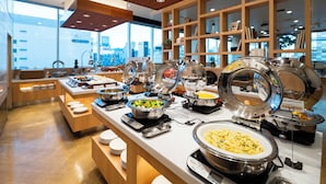 A buffet setup with various food stations, including pasta and salad, in a modern hotel setting with wooden accents and large windows. - Lotte City Hotel Kinshicho (Tokyo)