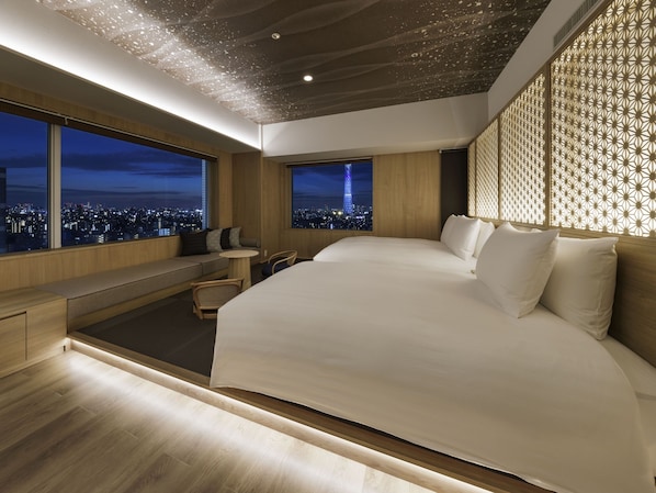 Una habitación de hotel moderna con una cama grande, zona de estar y vistas a la ciudad.