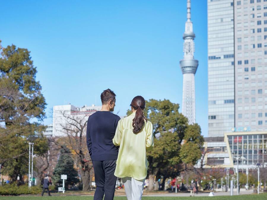 A couple walking in a park with a tall tower in the background.