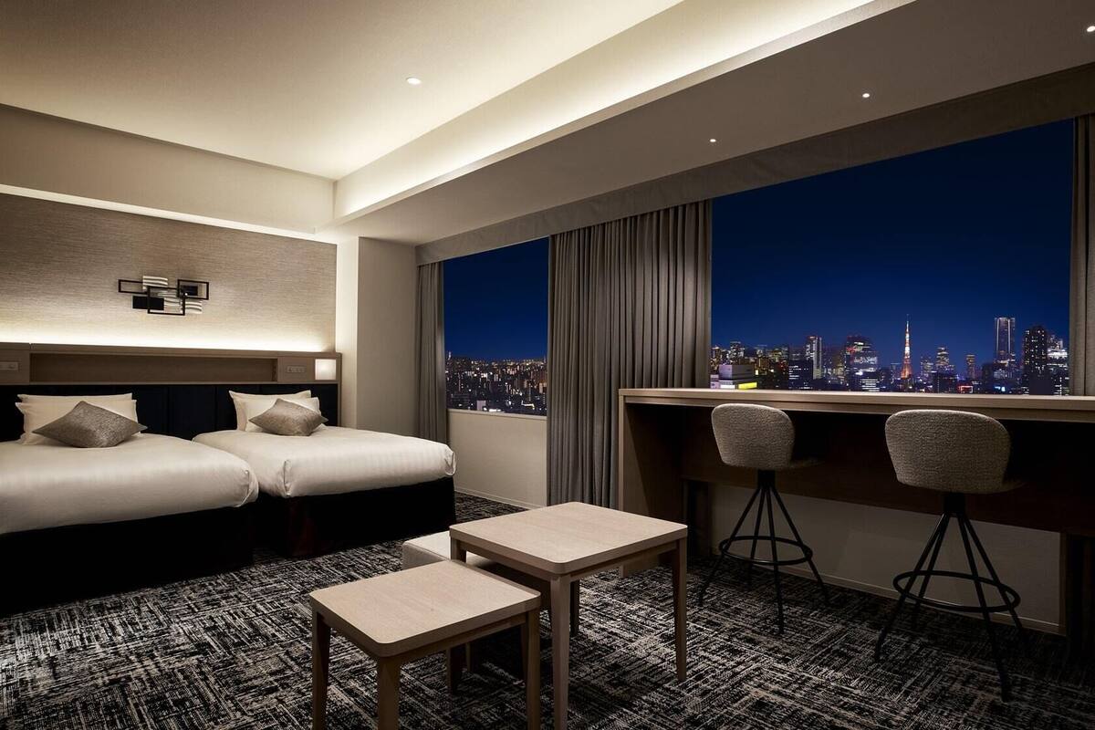 A hotel room with two beds, a desk with two chairs, a small table, and a city view.