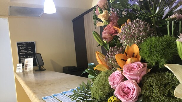 Un comptoir d’accueil agrémenté d’un arrangement floral, un panneau d’affichage indiquant les tarifs des chambres et un panneau signalant la disponibilité du Wi-Fi.
