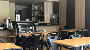 Un restaurant avec des tables en bois et des chaises noires, un appareil à café et un tableau affichant le menu.