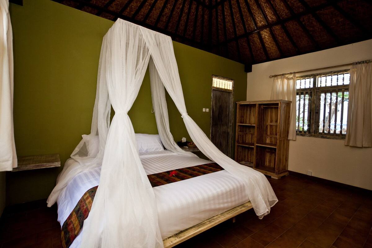 A four-poster bed with a canopy, a wooden wardrobe, and a window with curtains.