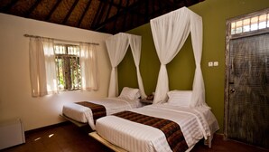 A room with two beds, each with white bedding and a canopy. There is a window with curtains, a radiator, and a door. - D Tunjung Resort & Spa (Karangasem)