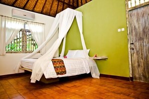 A single bed with a canopy in a room with a green wall, a wooden door, and a window with curtains.