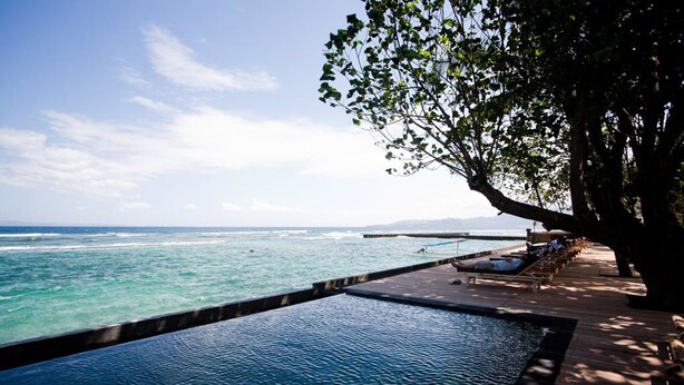 A infinity pool with a wooden deck and lounge chairs overlooking the ocean. - D Tunjung Resort & Spa (Karangasem)