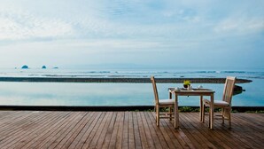 A wooden deck with a table and two chairs overlooking a calm sea with distant islands. - D Tunjung Resort & Spa (Karangasem)