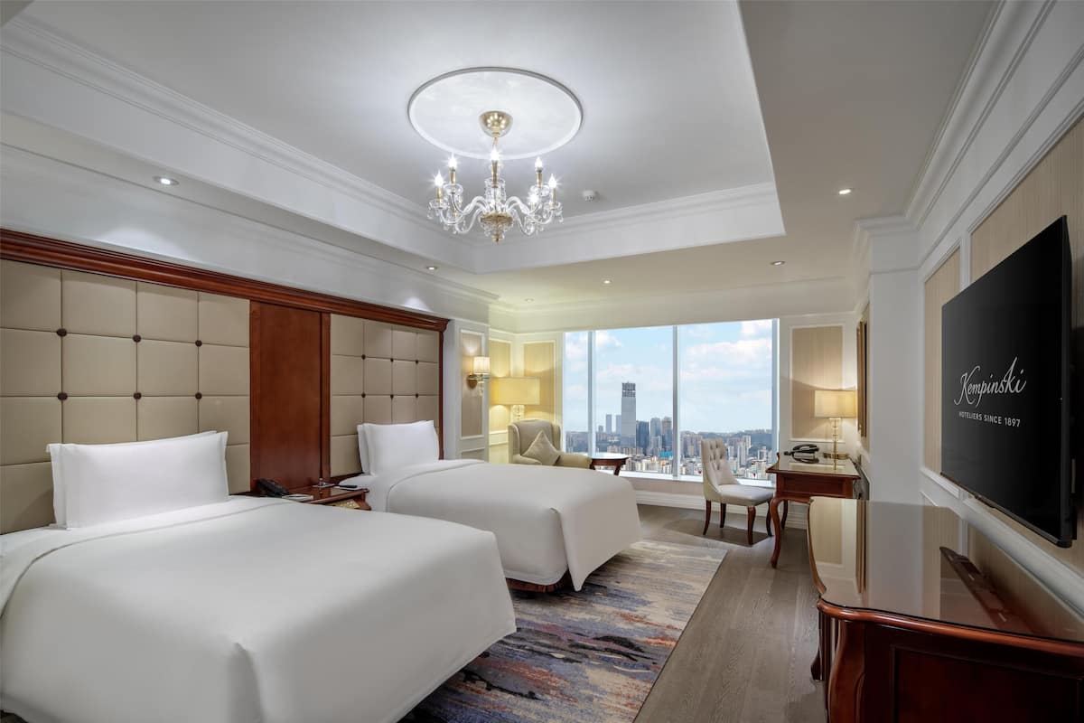 Ein Hotelzimmer mit zwei Betten, einem Kronleuchter, einem Fernseher und Blick auf die Stadt.
