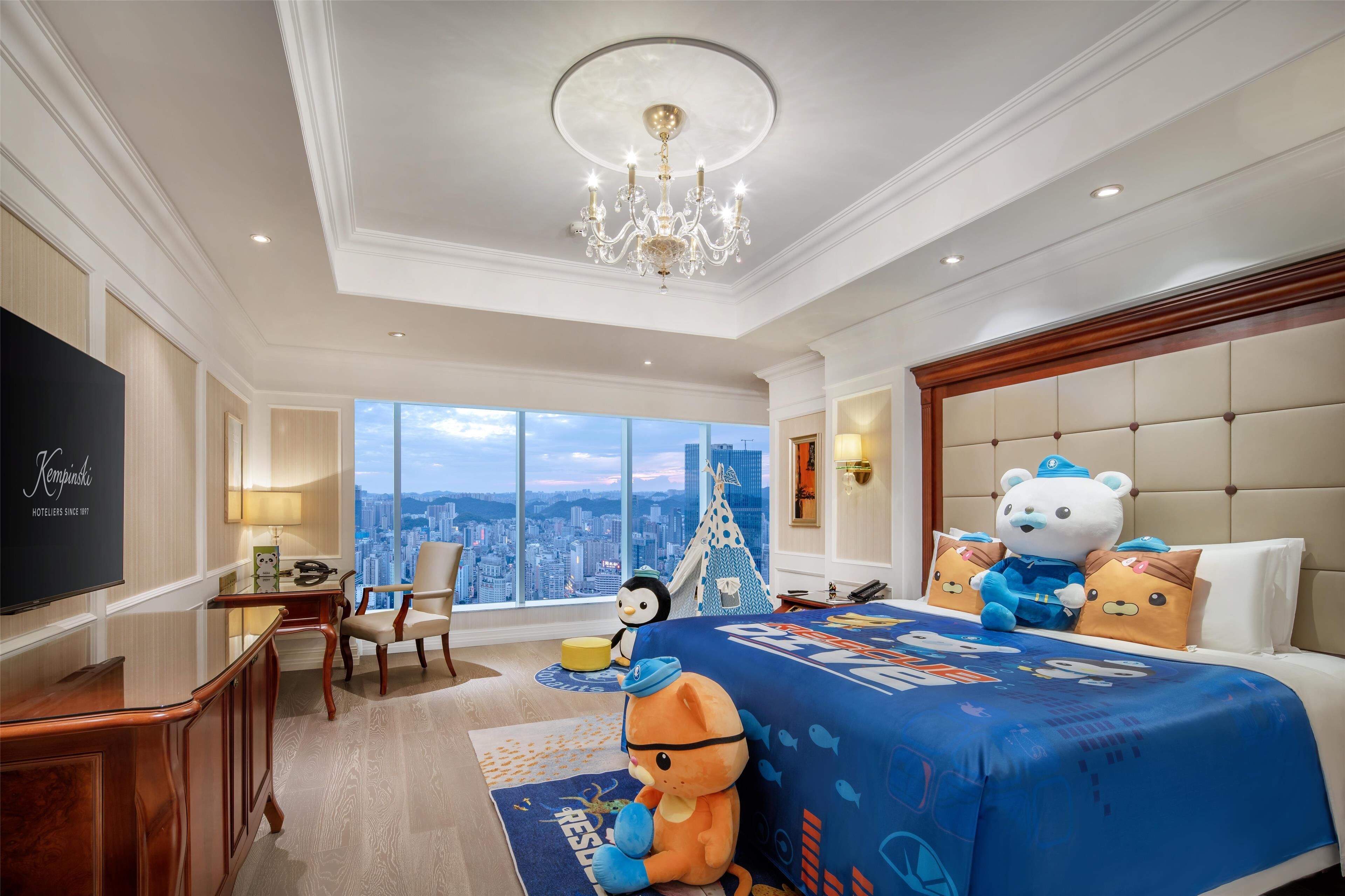 A hotel room with a large bed, a television, a desk, and a view of the city.