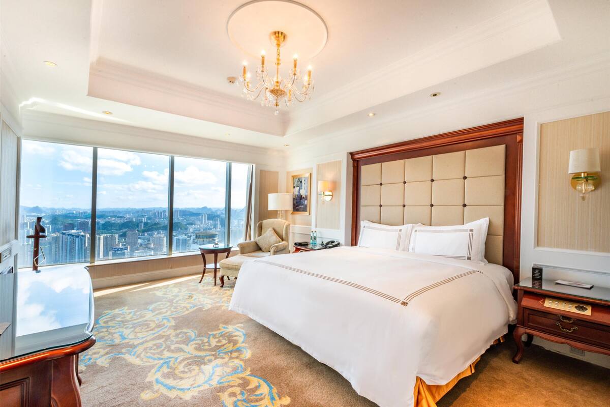 Ein geräumiges Hotelzimmer mit einem großen Bett, einer Sitzecke, Blick auf die Stadt und einem Chandelier.