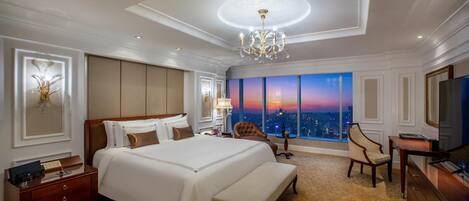 Une chambre d’hôtel spacieuse, dotée d’un grand lit, d’une banquette, d’une télévision et offrant une vue sur la ville au coucher du soleil.