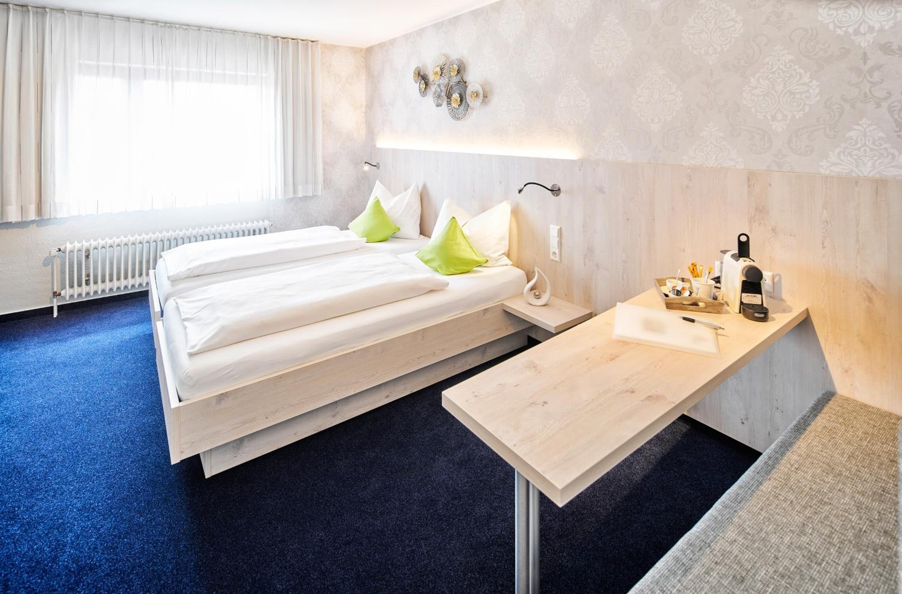 A hotel room with a bed, bedside table, and a small desk with a chair.