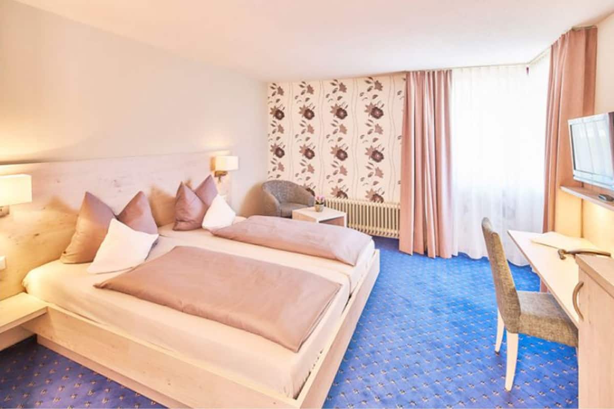 Habitación de hotel con una cama grande, un escritorio, una silla, un televisor y una ventana con cortinas.