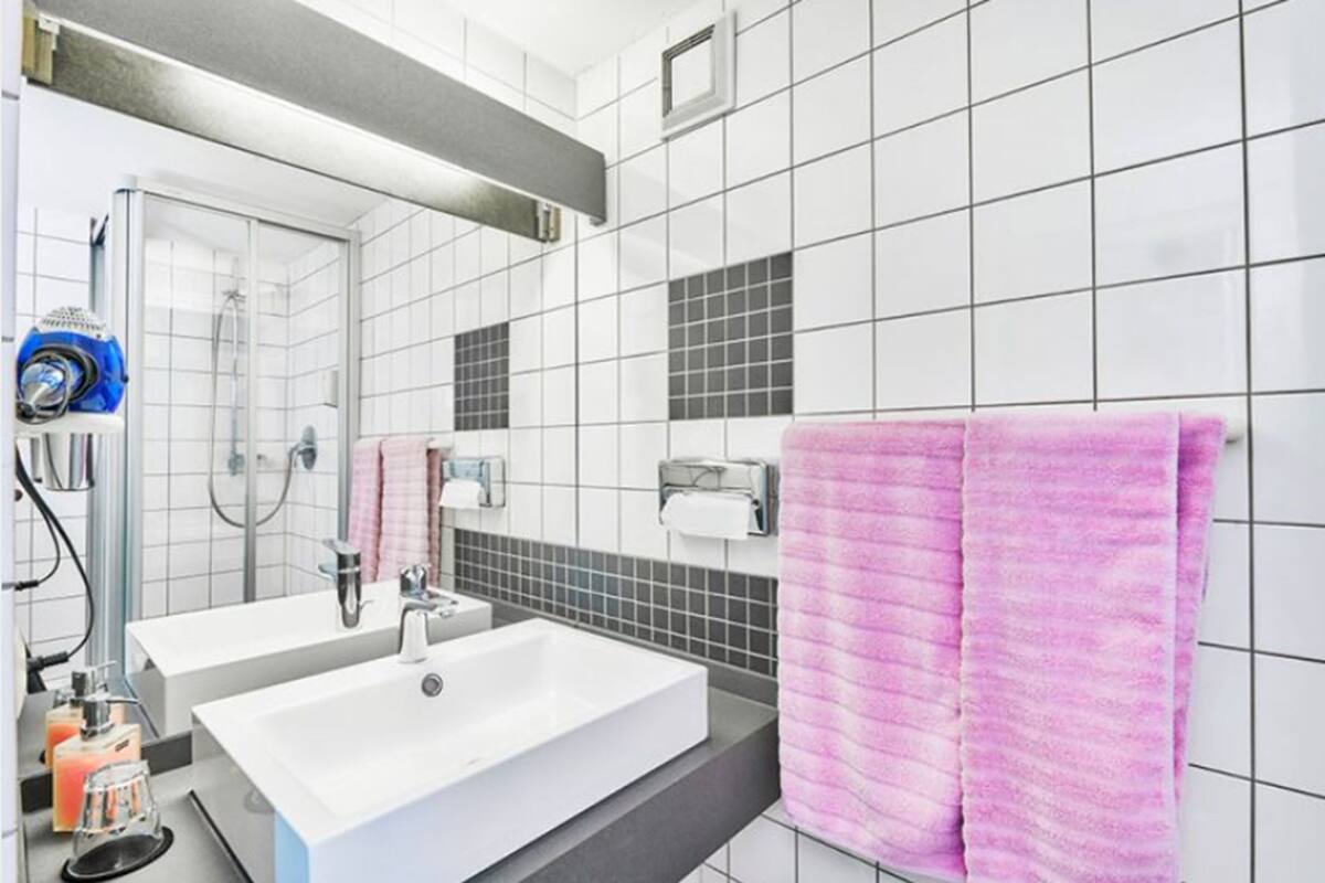 Un baño moderno con dos lavamanos, una ducha y un toallero con toallas rosas.