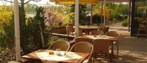 An outdoor patio with tables and chairs, covered by a white canopy.