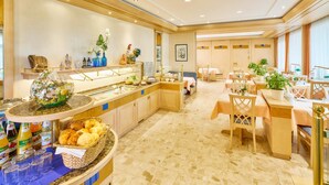 Espaço de café da manhã de hotel com buffet, incluindo diversos alimentos e bebidas.