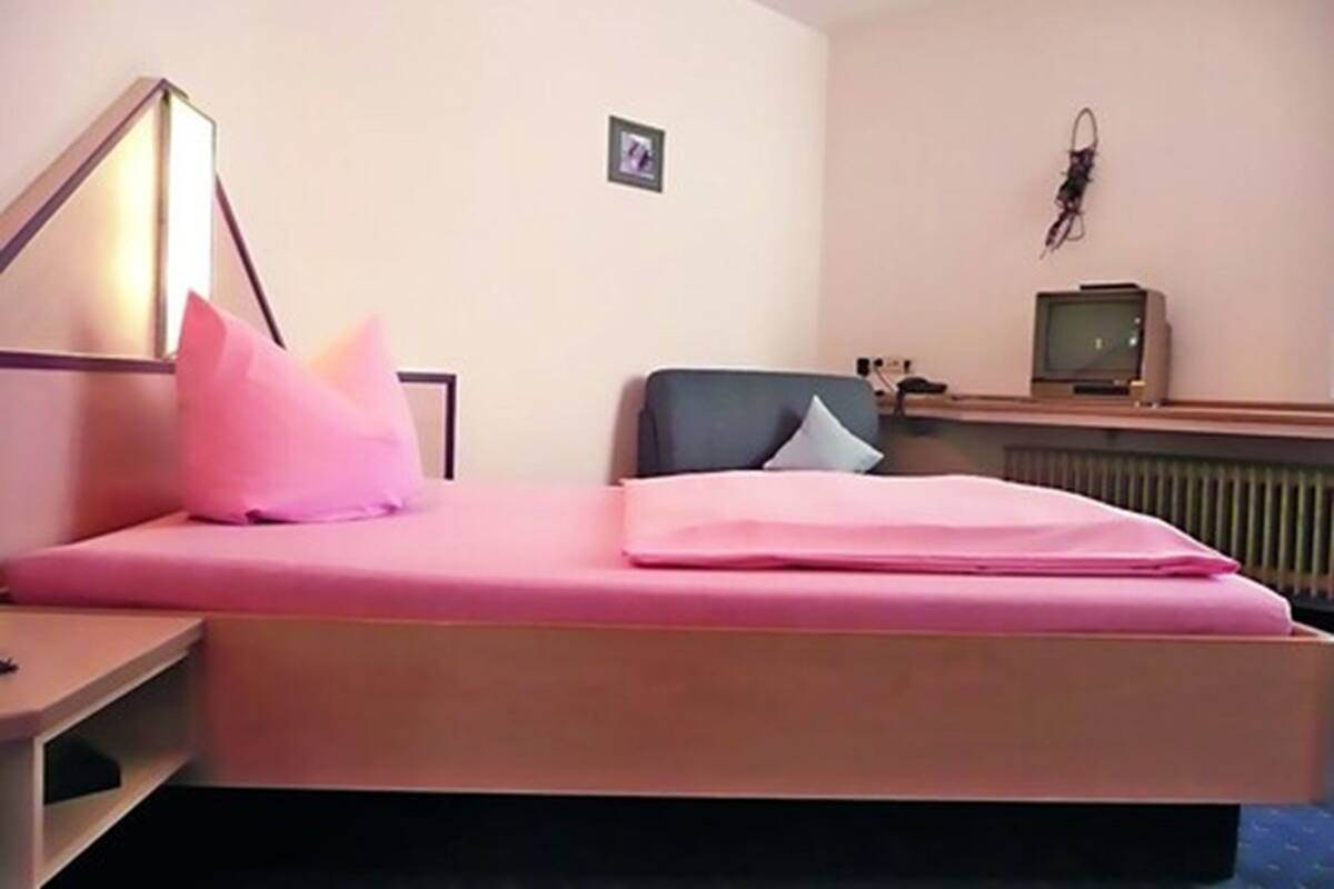 Un dormitorio con cama, escritorio, silla, televisor y un cuadro en la pared.