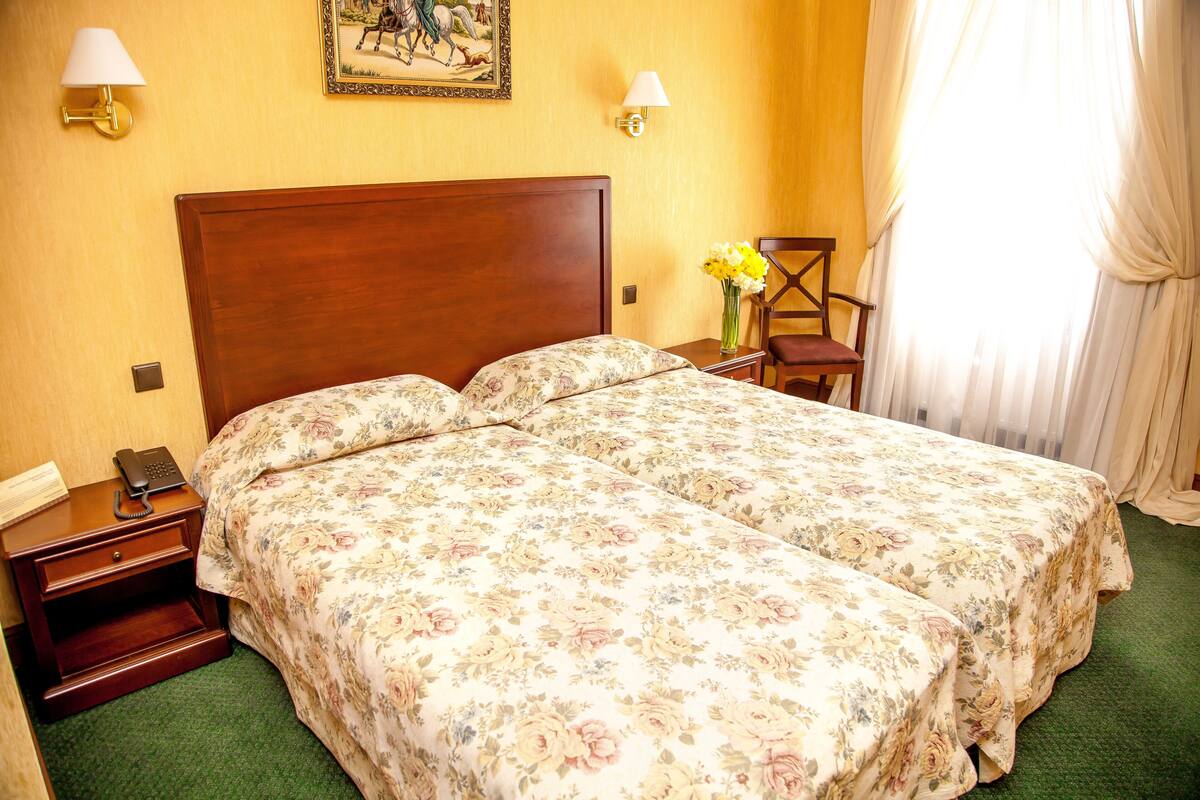 A hotel room with two beds, a nightstand with a telephone, a chair, and a vase with flowers.