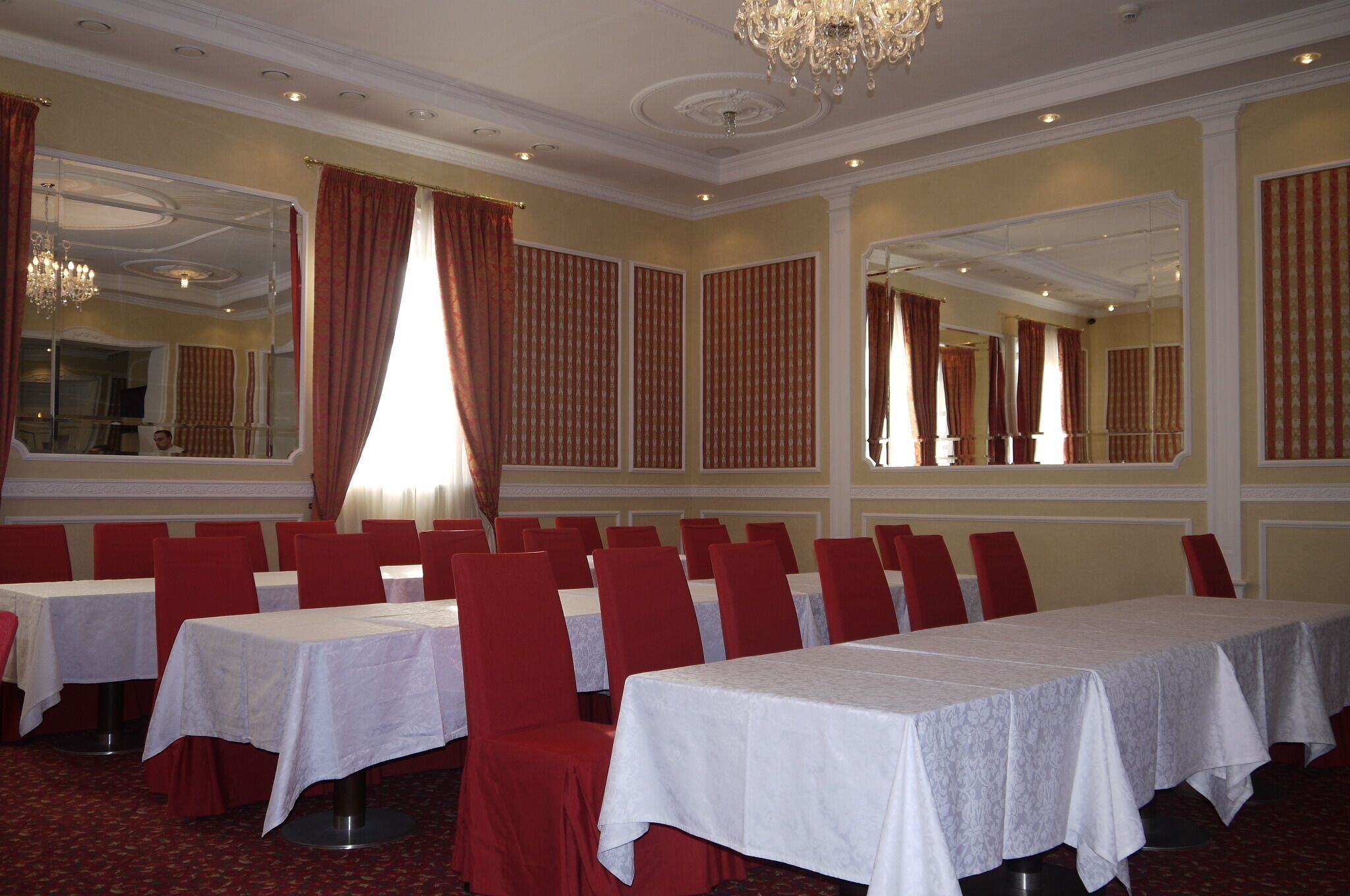 A banquet hall with multiple tables and chairs, large mirrors, and a chandelier.