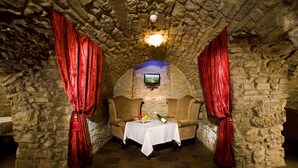 A stone-walled room with a table set for two, featuring a bottle and fruit. - Optima Collection Kamianets-Podilskyi (Kamianets-Podilskyi)