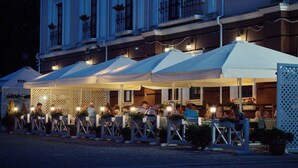 An outdoor dining area with multiple tables and umbrellas, surrounded by a white fence and potted plants. - Optima Collection Kamianets-Podilskyi (Kamianets-Podilskyi)