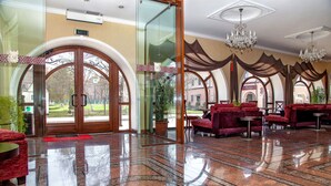 A hotel lobby with a grand entrance, red upholstered seating, and a chandelier. - Optima Collection Kamianets-Podilskyi (Kamianets-Podilskyi)