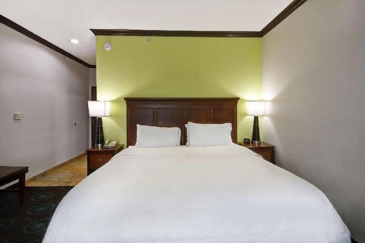 Ein Hotelzimmer mit einem großen Bett, zwei Nachttischlampen, einem hölzernen Kopfteil und einem Telefon auf dem Nachttisch.