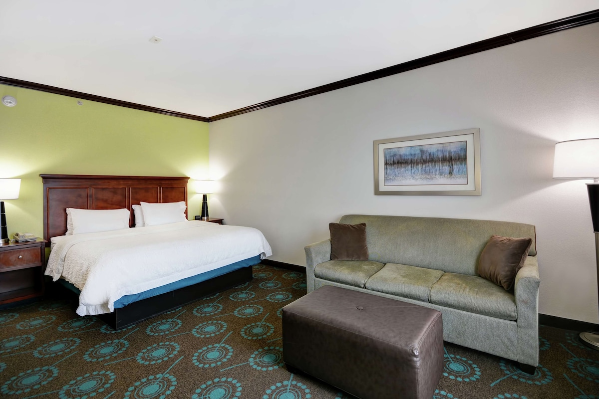 Ein Hotelzimmer mit Bett, Sofa, Hocker und einem Gemälde an der Wand.