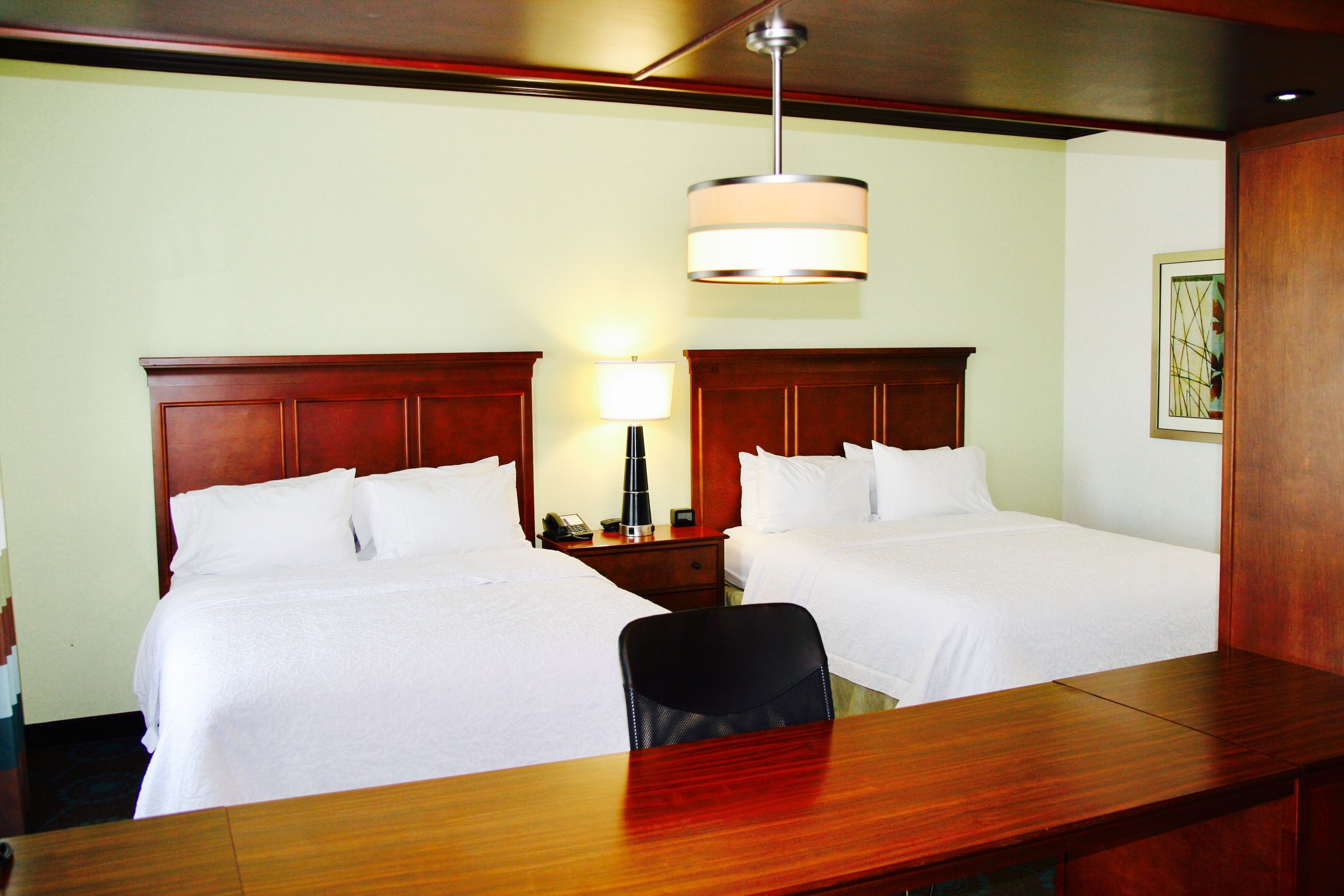 Une chambre d’hôtel avec deux lits, un bureau en bois, une lampe et un tableau au mur.