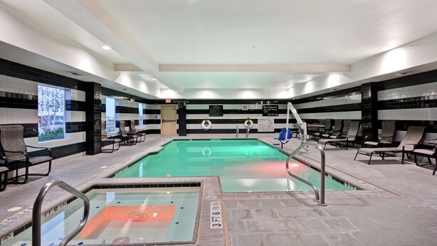 Ein Poolbereich mit Liegestühlen, einem Rettungsschwimmer-Schild und klarem Wasser.