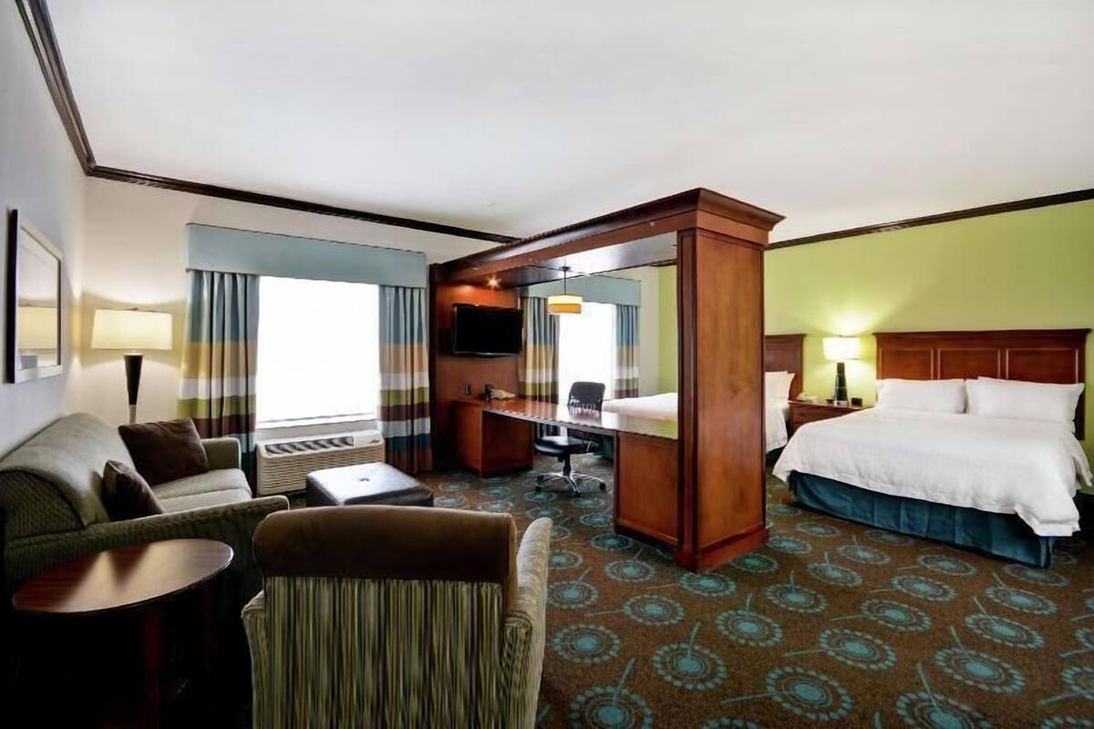 Ein Hotelzimmer mit Bett, Schreibtisch, Stuhl, Sofa und Fernseher.