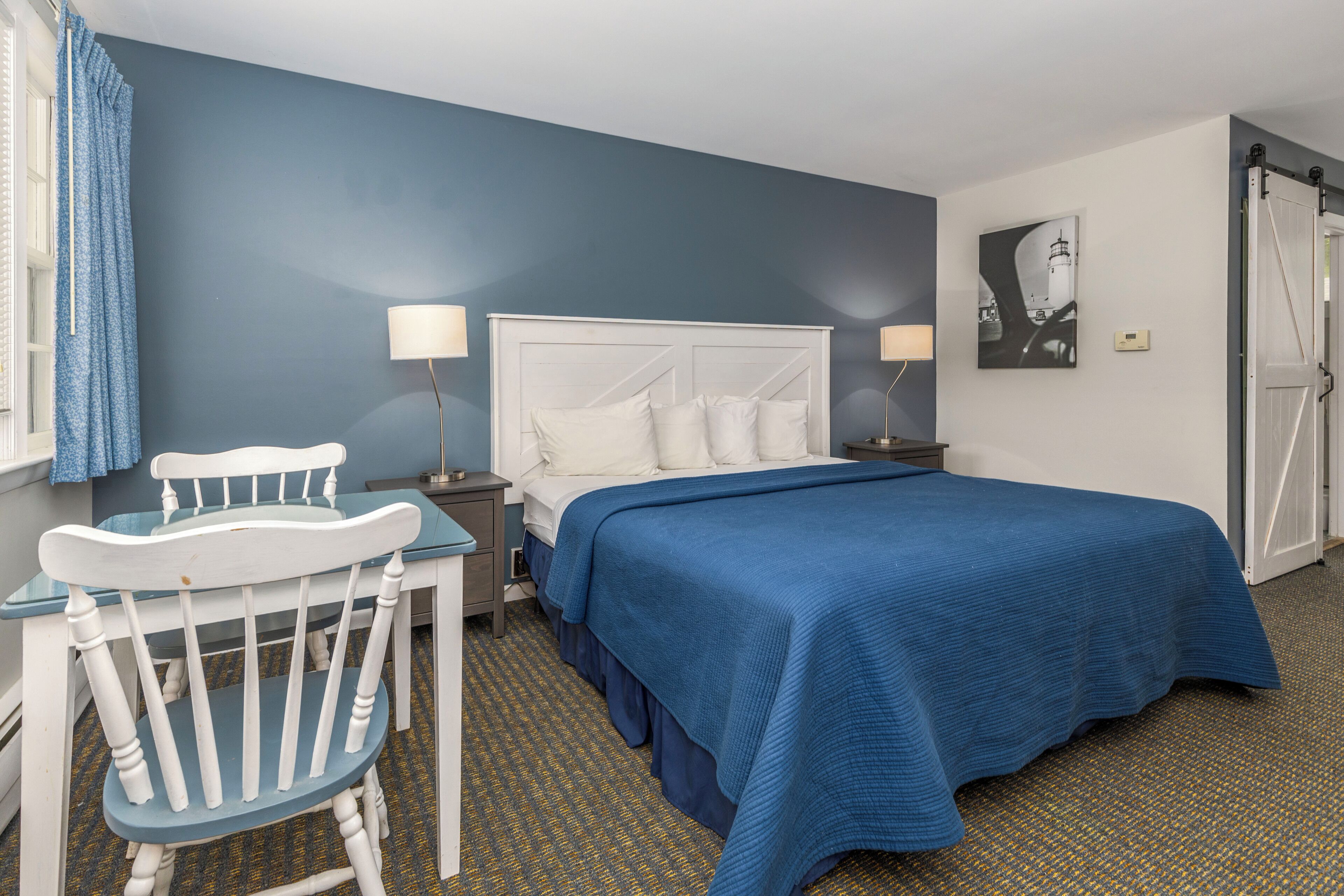 A hotel room with a bed, a chair, a table, and a lamp.