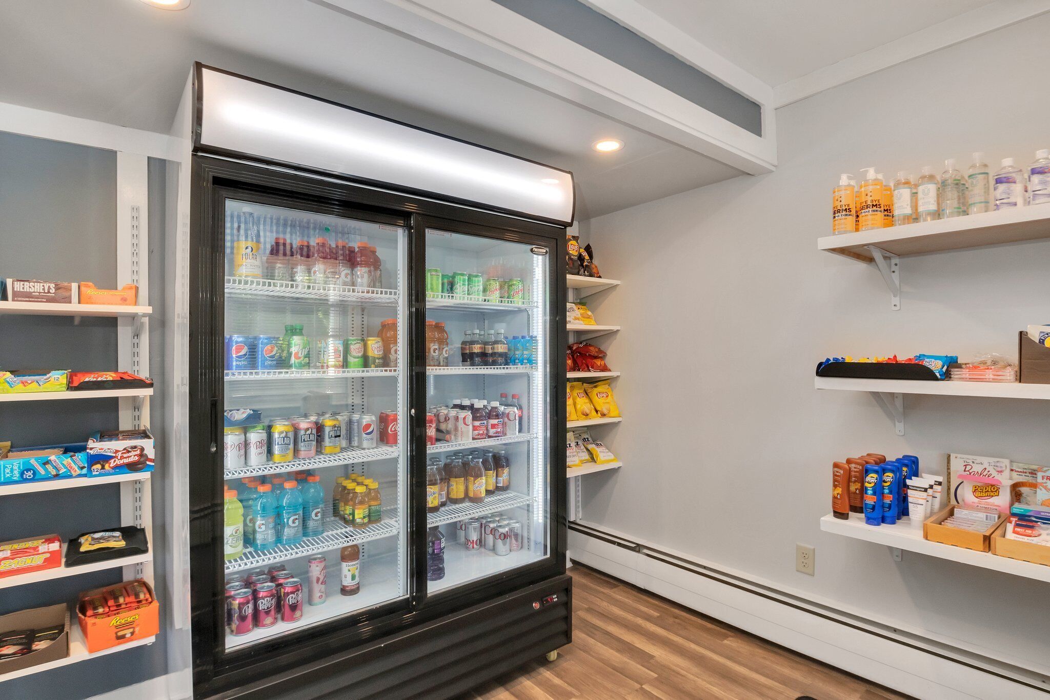 Mostrador refrigerado repleto de diversas bebidas e lanches, com prateleiras ao redor exibindo produtos adicionais.