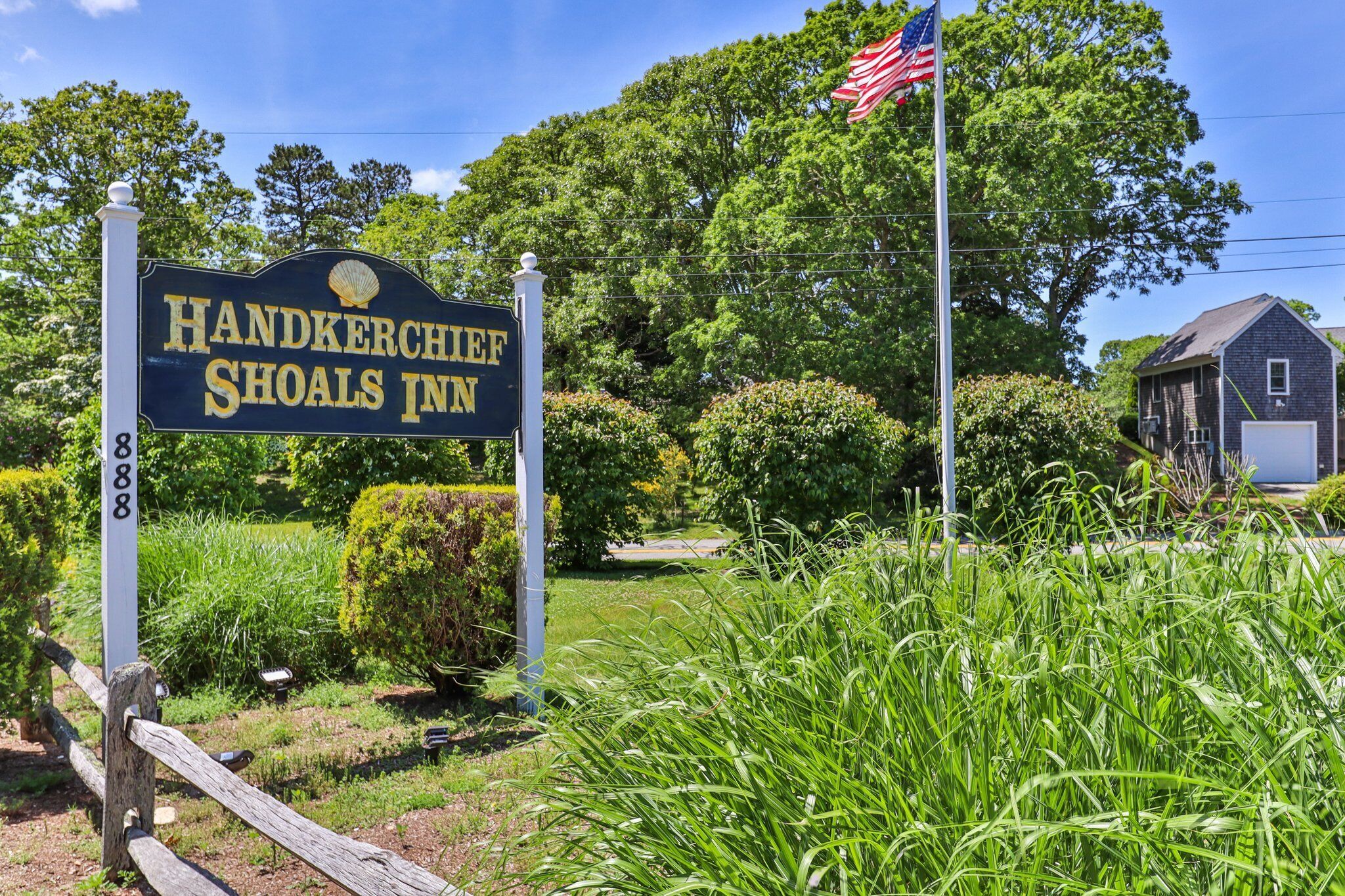 A sign for Handkerchief Shoals Inn with a flagpole and lush greenery in the background.