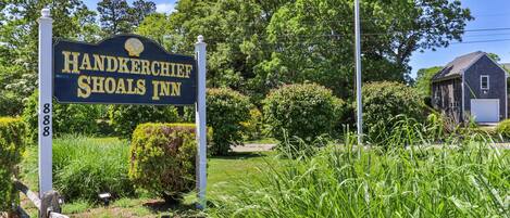A sign for Handkerchief Shoals Inn with a flagpole and lush greenery in the background.
