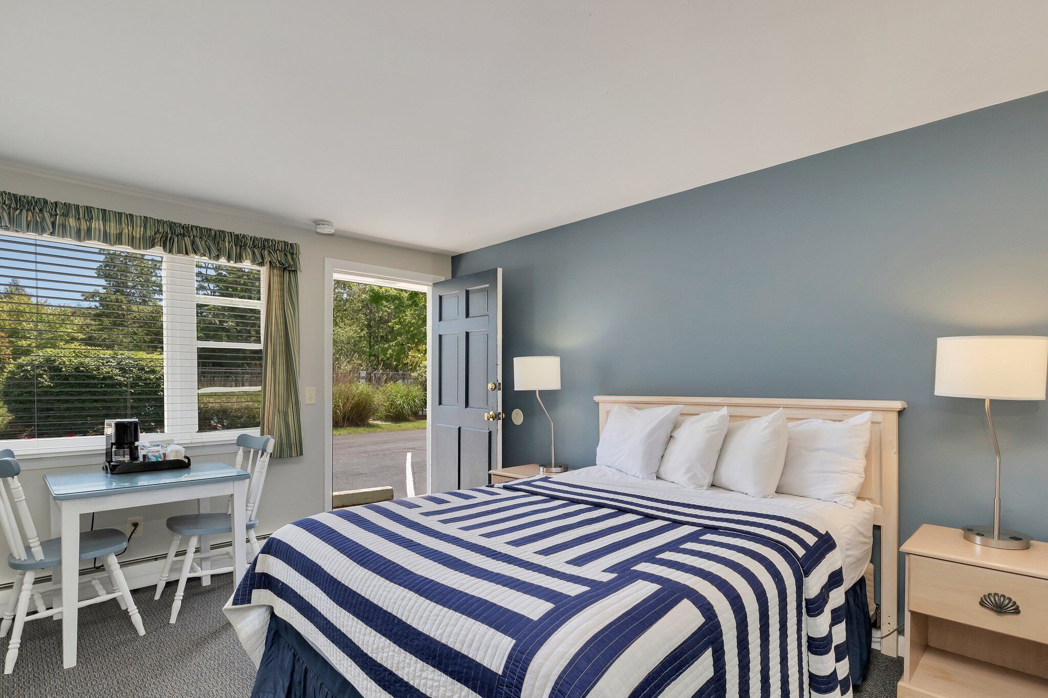 Habitación de hotel con cama, mesitas de noche, escritorio con silla y ventana con cortinas.