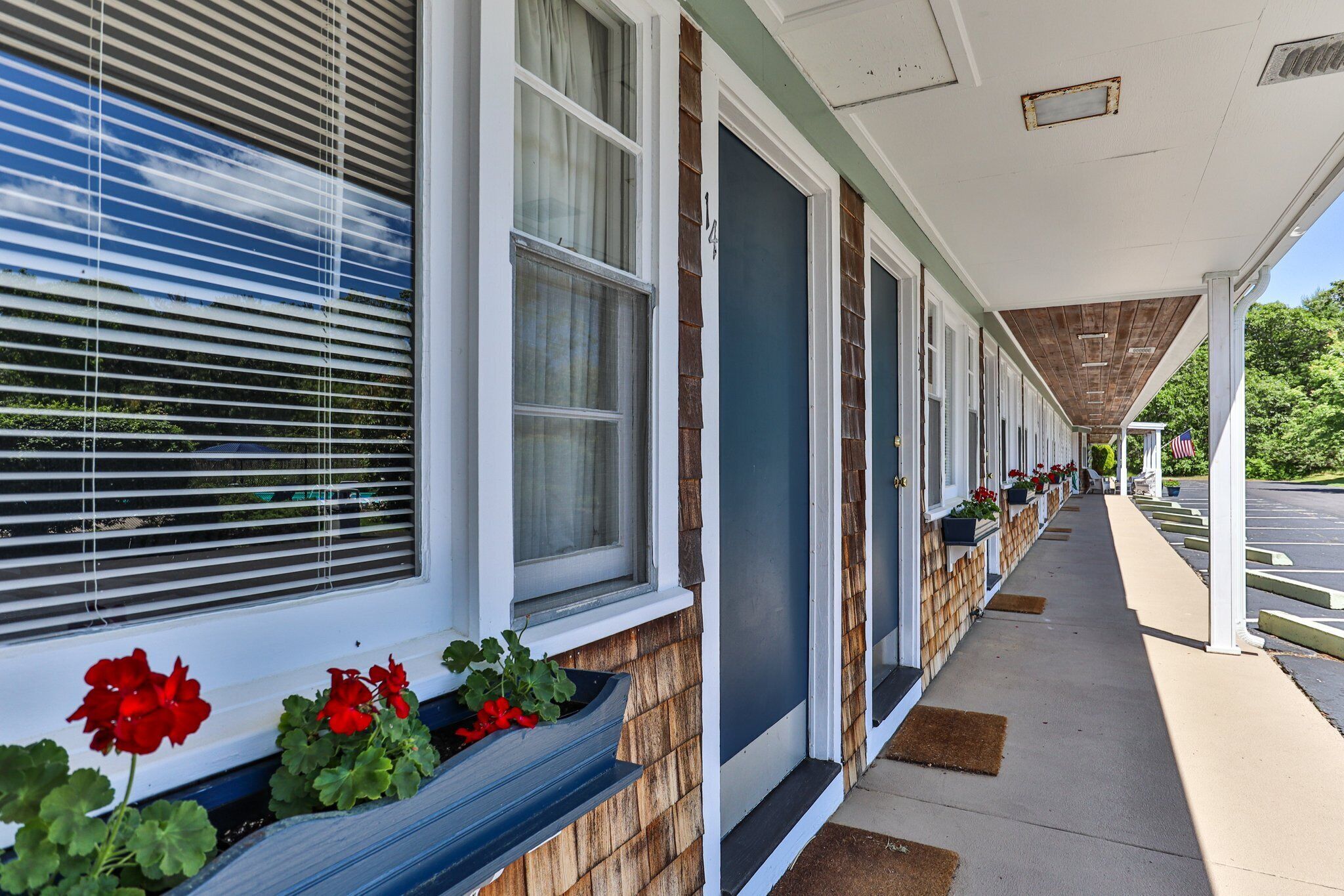 A row of motel rooms with large windows, a covered walkway, and a parking lot in the background.