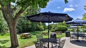 Une terrasse extérieure avec des tables et des chaises rondes, des tables de pique-nique et des parasols.