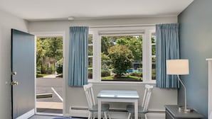 Une chambre à coucher avec un lit, une table, deux chaises, une lampe et une fenêtre avec des rideaux.