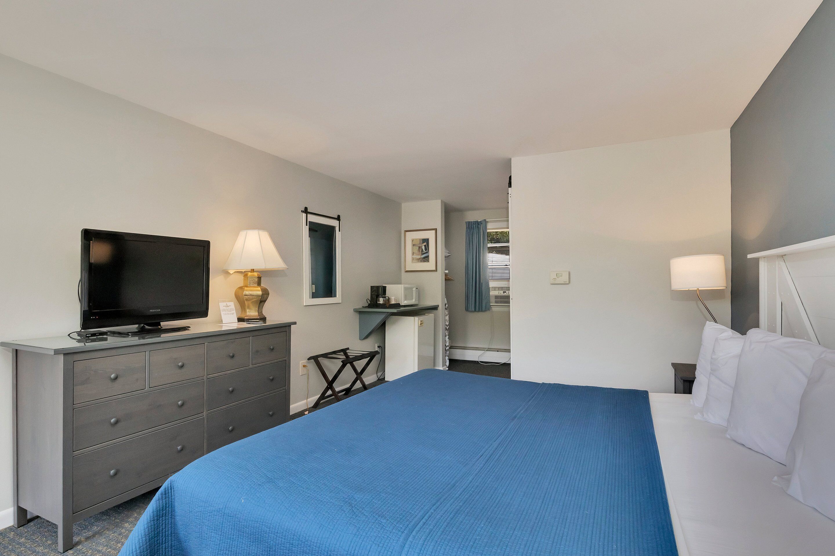 Ein Hotelzimmer mit Bett, Fernseher auf einer Kommode, Schreibtisch mit Stuhl und einem Fenster mit Vorhängen.