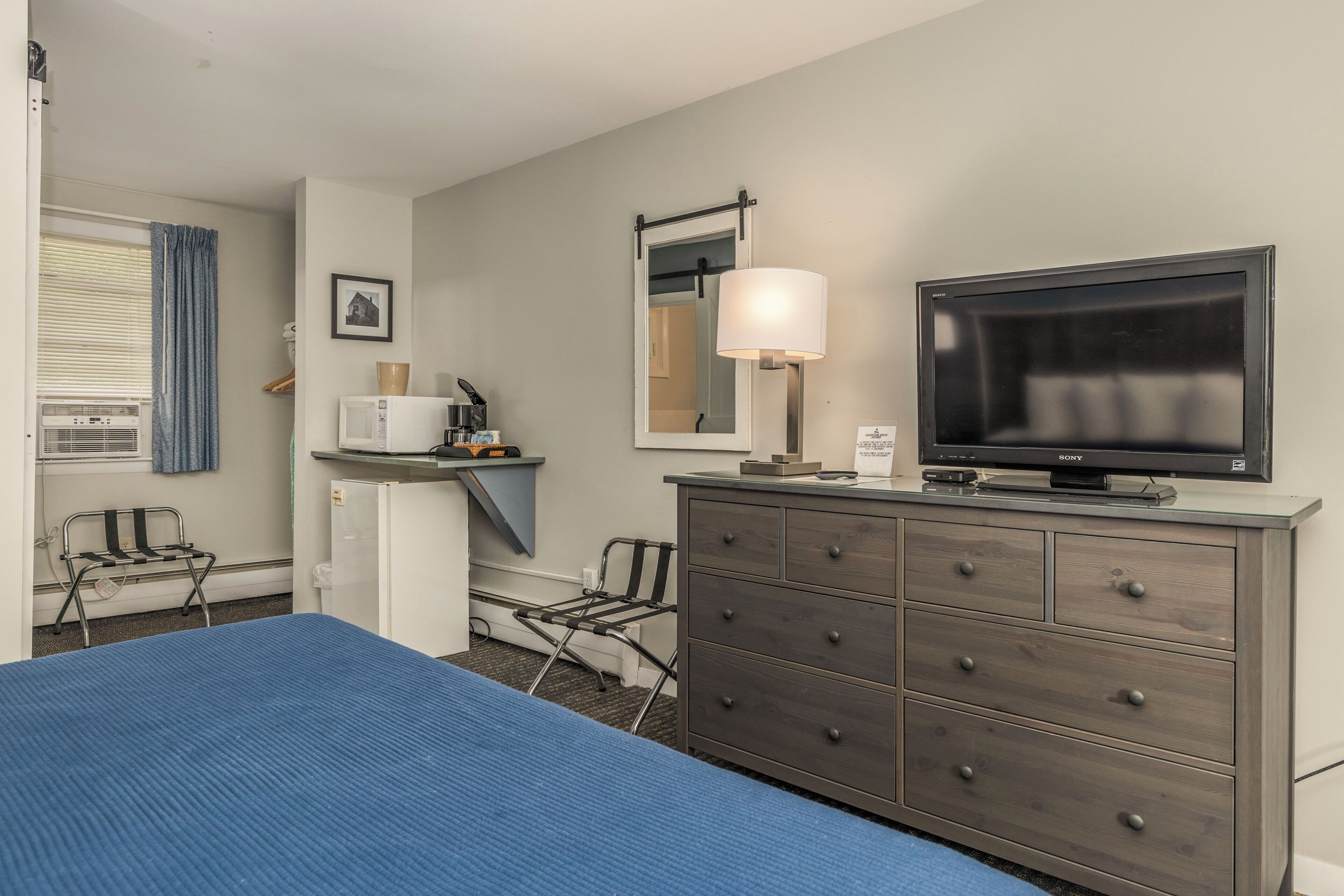 Una habitación de hotel con cama, cómoda, televisor, microondas y una silla.