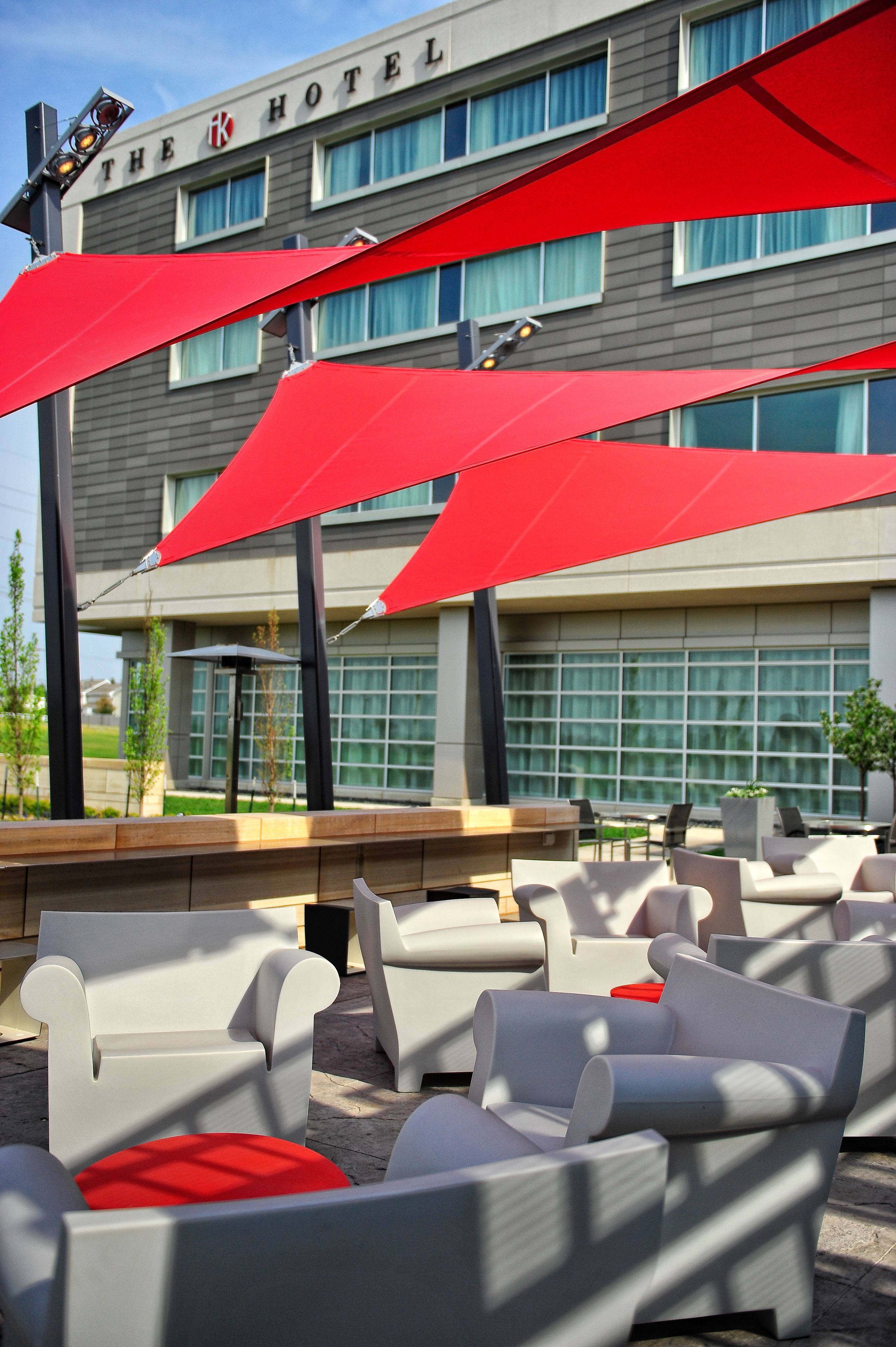 Exterior de hotel com área de estar ao ar livre e guarda-sóis vermelhos.