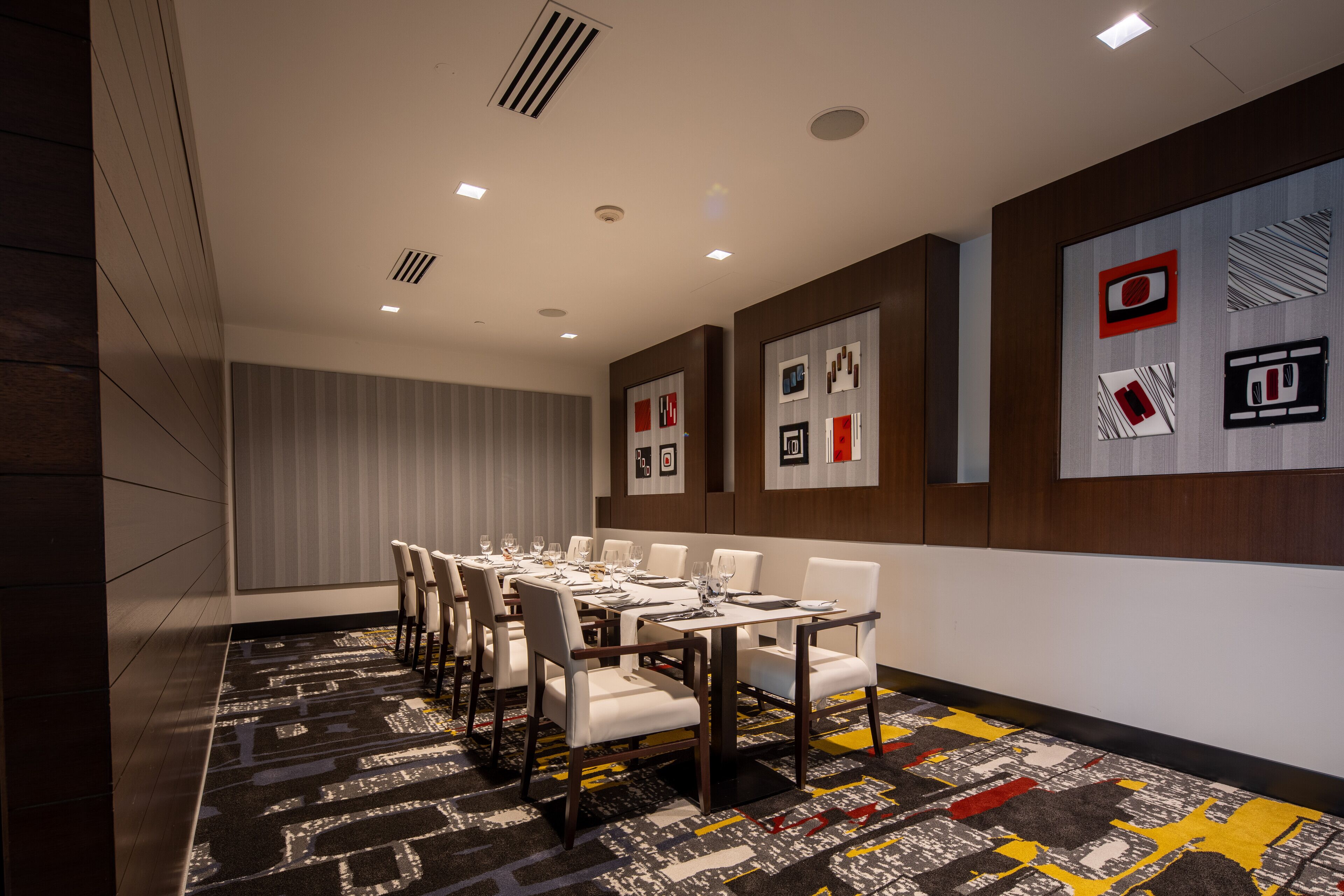 A conference room with a long table, white chairs, and a patterned carpet.