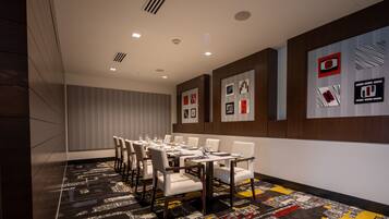 A conference room with a long table, white chairs, and a patterned carpet.